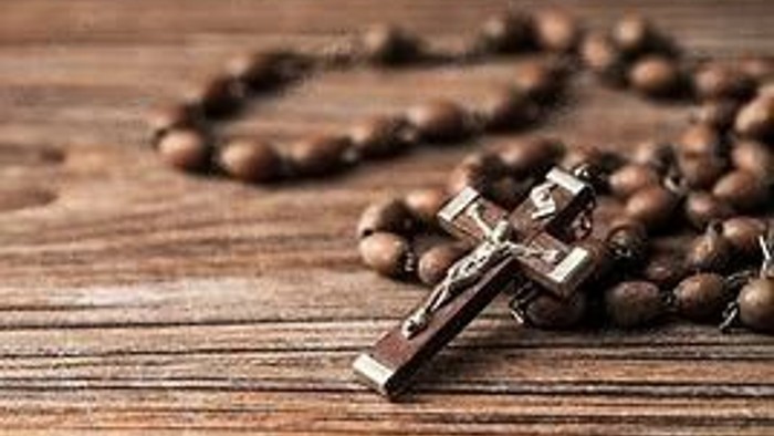 Ein Kreuz mit Rosenkranz auf einem Holztisch.