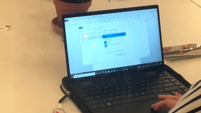 En gruppe af voksne sidder ved et bord med vin og en laptop.