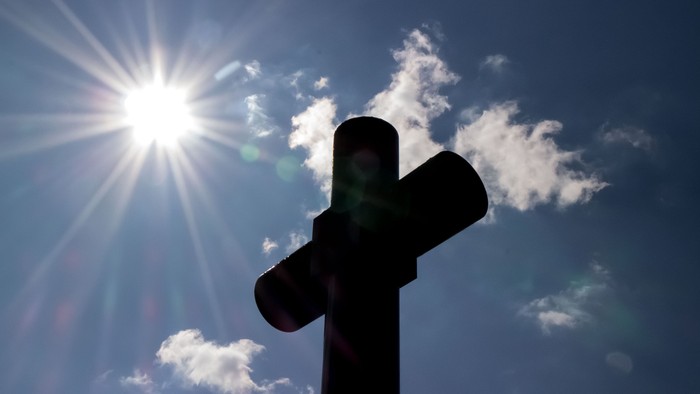 Ein Kreuz vor einem sonnenstrahl durchzogenen Himmel
