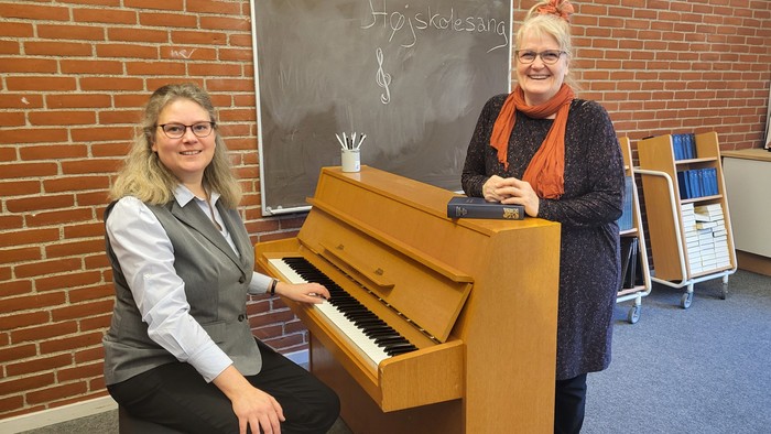 To da kvinder sidder ved et piano i en klassesal.