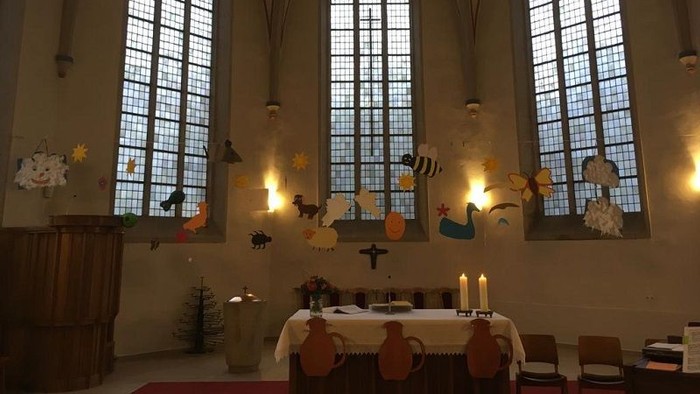 In der Kirche stehen ein Tisch mit Kerzen und Weihnachtsdekorationen vor drei hohen Fenstern.