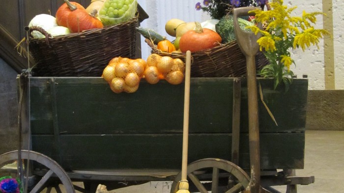 Kutsche mit Gemüse und Blumen vor weißer Wand