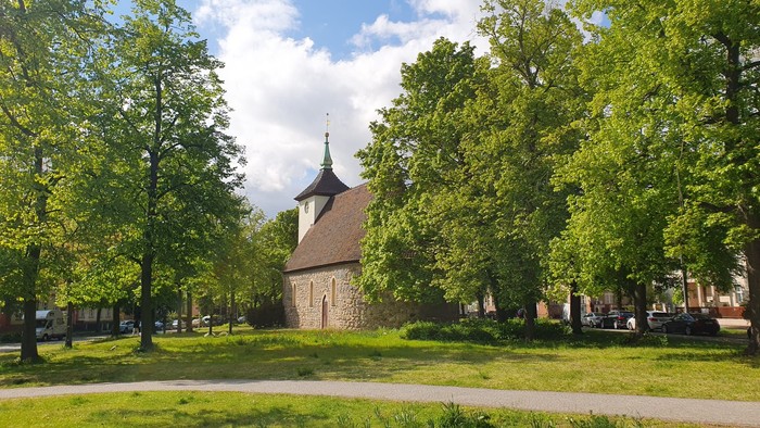 Historische Steinkirche, eingebettet zwischen üppigen grünen Bäumen in einer ruhigen, parkähnlichen Umgebung.