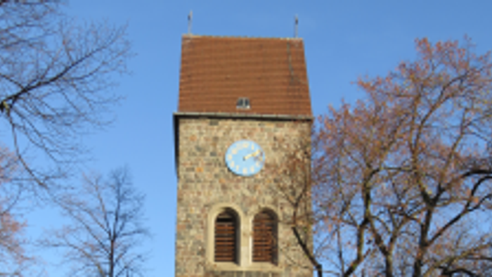 Alter Kirchturm mit Uhr und buntem Glasfenster, umgeben von Bäumen