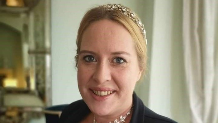 En kvinde i mørkt jakkesæt med halsbånd og hårbånd.