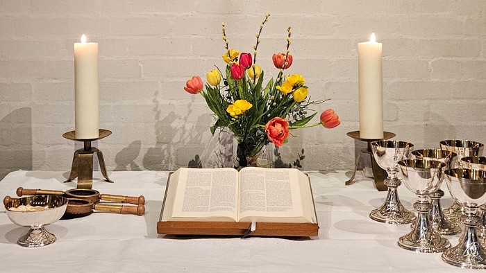 Ein Tisch mit Kerzen, Blumen und einem Buch vor einer Ziegelwand