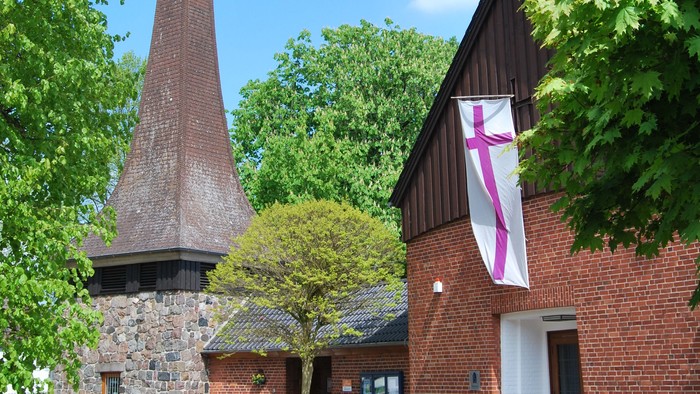 Das Bild zeigt ein Ziegelgebäude mit einem hohen Schornstein und einem Kreuzbanner.