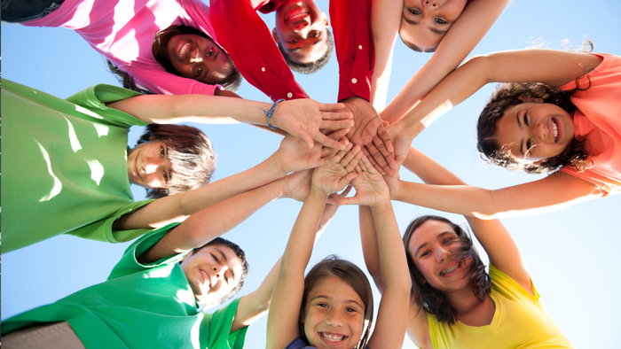 Ein Gruppenfoto von Kindern mit erhobenen Händen, die ein farbenfrohes Banner halten, mit dem Text "THOMASKIRCHE KÖLN"