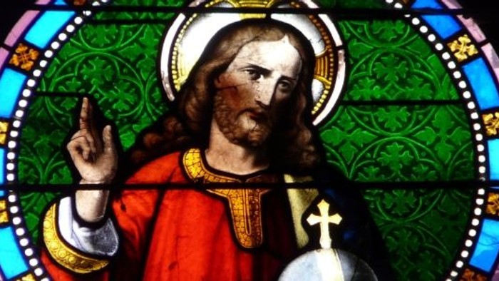 Farvet glasafbildning af Jesus Kristus, der velsigner med en glorie og religiøse symboler.