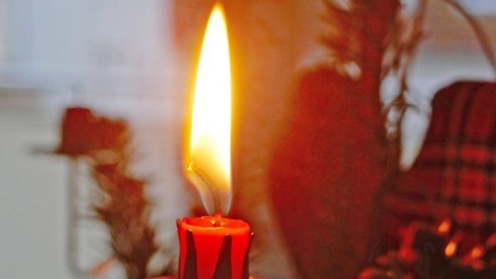 Eine brennende rote Kerze steht auf einem Tannenzapfen.