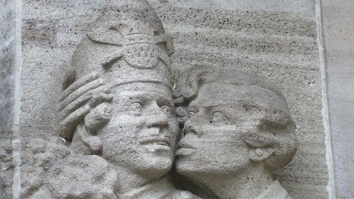 Die Steinrelief zeigt zwei Personen mit Kopfbedeckungen.