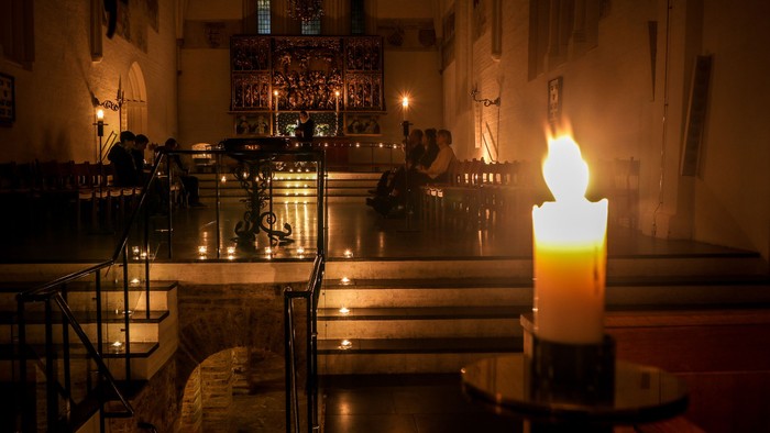 En kirkeinterior med lysende lysstaker og en lysende stearinlys i forgrunden