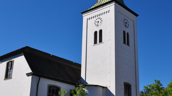 Eine malerische weiße Kirche mit hohem Turm und grüner Spitze vor einem klaren blauen Himmel.