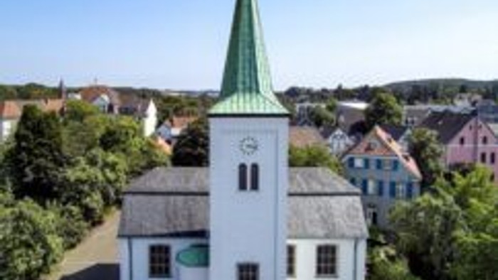 Luftaufnahme einer malerischen weißen Kirche mit grünem Turm in einer kleinen, idyllischen Stadt.