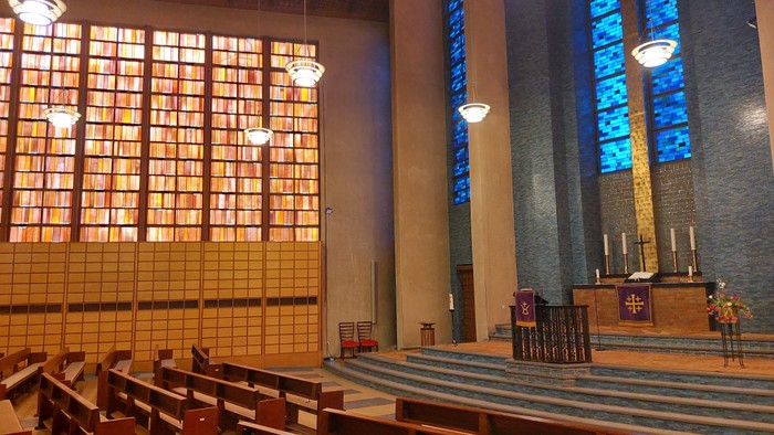 Moderne Kircheninnenausstattung mit Buntglasfenstern, hölzernen Kirchenbänken und einem ruhigen Altarraum.