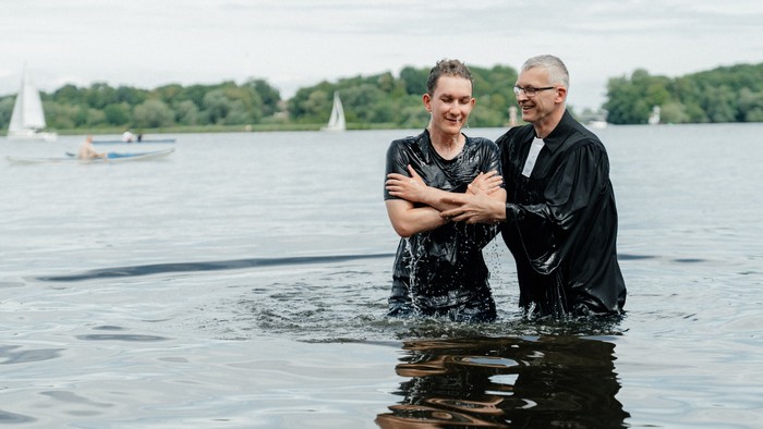 Zwei Männer in dunkler Kleidung stehen im Wasser und lächeln.