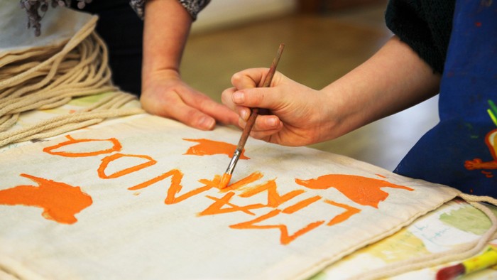 Eine Person malt mit orangefarbener Farbe das Wort