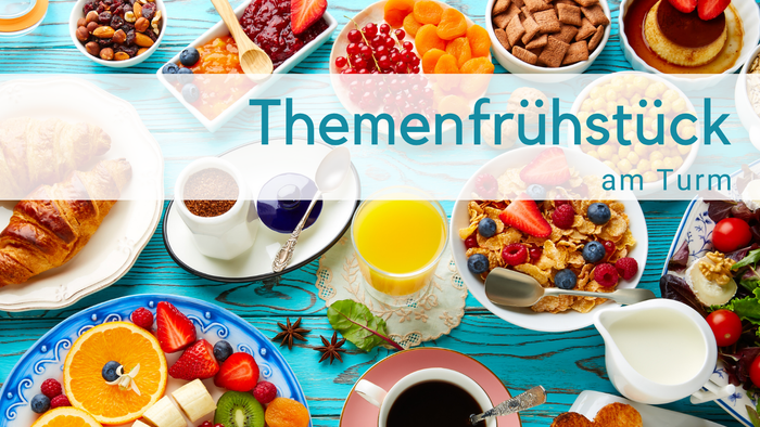 Hellblauer Holztisch mit Frühstückszutaten: O-Saft, Milchkännchen, obst, Cerealien, Tomaten, Croissant, Törtchen