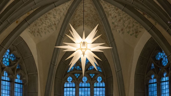 Große weiße Stern-Dekoration, die in einer prächtigen Kathedrale mit hohen Buntglasfenstern hängt.