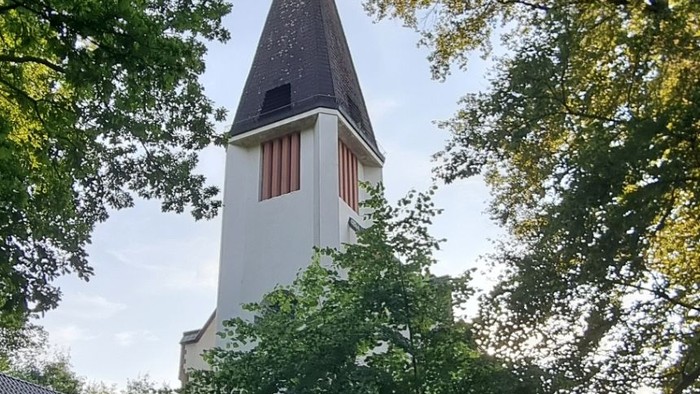 Weiße Kirche mit hohem Kirchturm, umgeben von Bäumen.