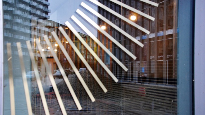 Glasfasade med refleksion af lysstokke og bygning.