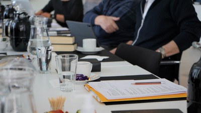 En gruppe af mennesker sidder ved et bord med notatblokke, penner og laptopter.