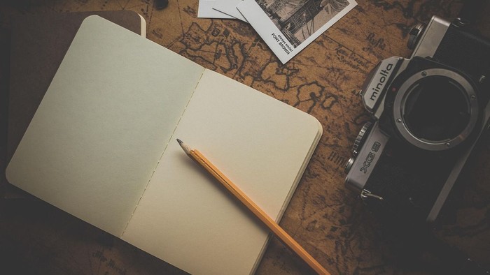 Offenes Notizbuch mit Bleistift, Kamera und Postkarten auf einer Landkarte