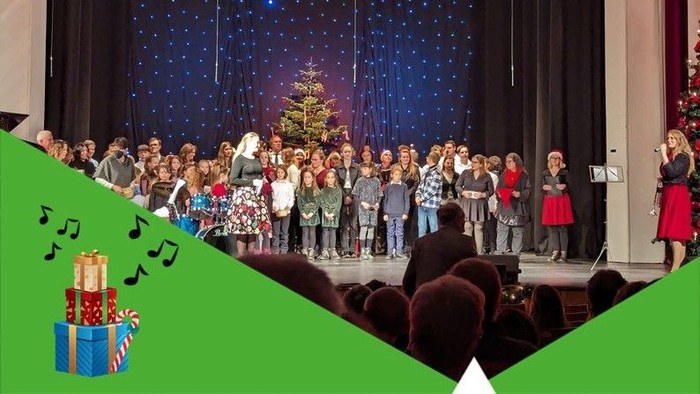 Eine Gruppe von Kindern singt auf einer Bühne vor einem Weihnachtsbaum und einem blauen Vorhang
