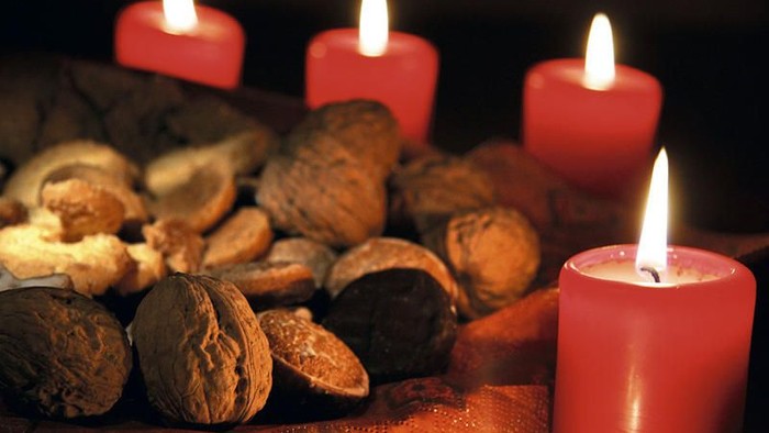 Drei brennende rote Kerzen umgeben eine Sammlung von Walnüssen.