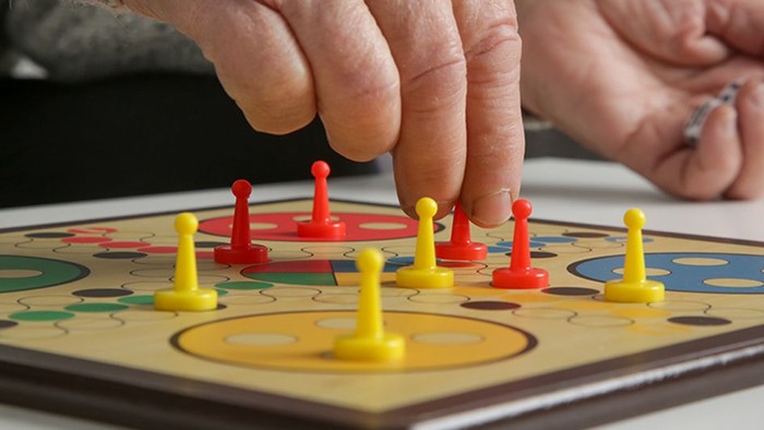 Eine Person spielt ein Brettspiel mit gelben und roten Figuren.