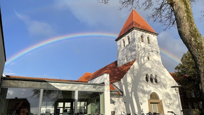 En regnbue over et hvidt kirkebygning med røde tag.