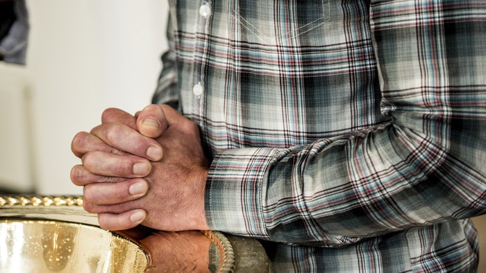 En person i en ternet skjorte med foldede hænder, der hviler på et bord.