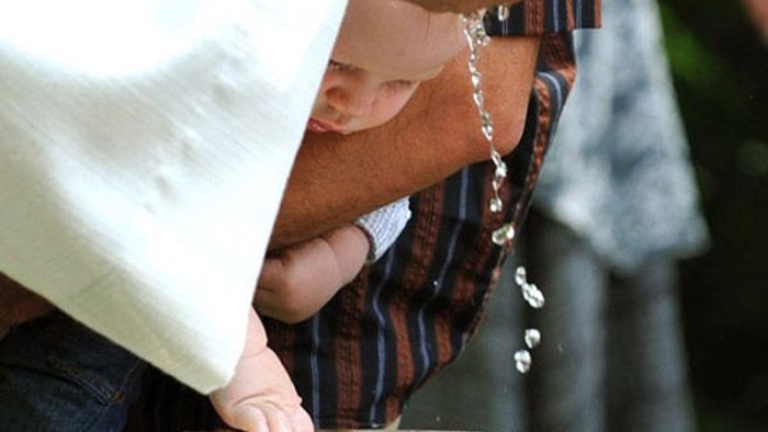 Eine Person segnet sich mit Weihwasser aus einem Brunnen, während sie einen Rosenkranz hält.