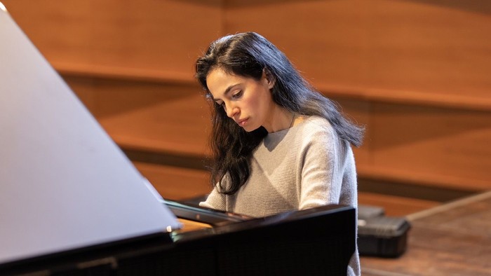 Eine Frau spielt konzentriert Klavier in einem warm beleuchteten Konzertsaal.