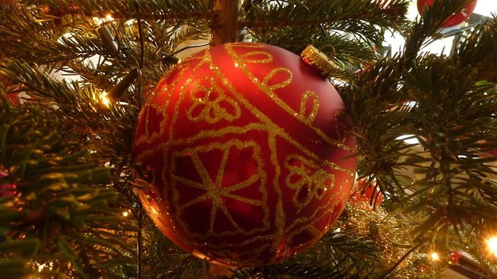 Roter Weihnachtschmuck mit goldener Verzierung hängt am Baum.
