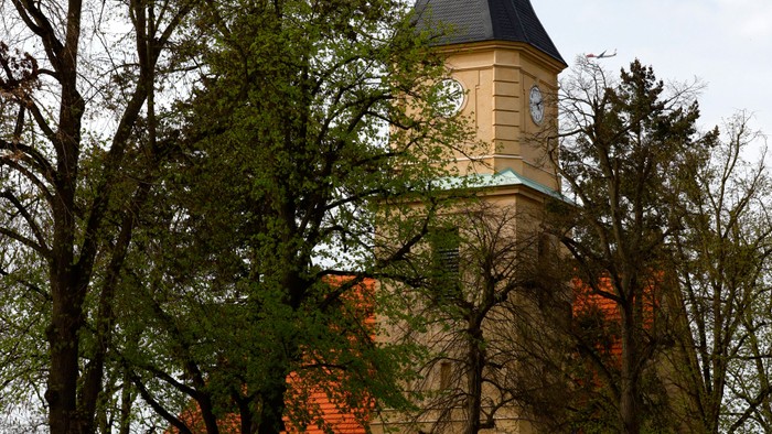 Ein Kirchengebäude mit hohem Turm und spitzem Dach, umgeben von Bäumen und Autos.