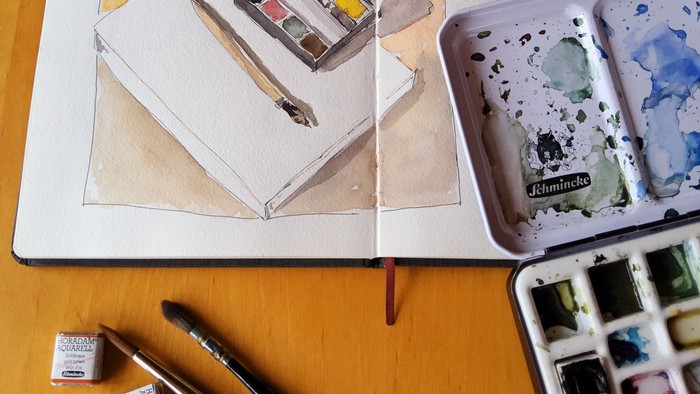 Ein Skizzenbuch mit Wasserfarben und Pinseln auf einem Holztisch