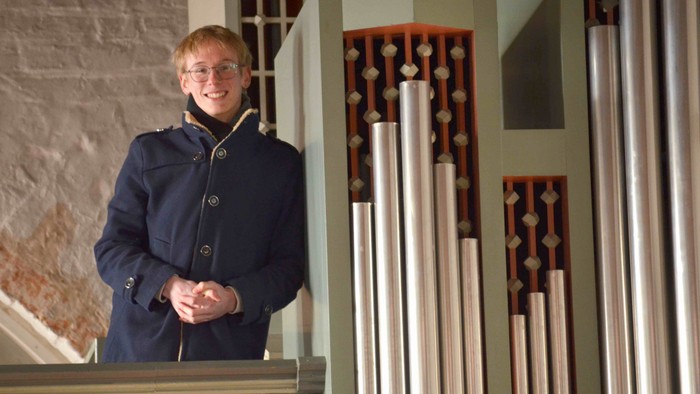 Ein Mann steht vor einem Orgelpfeifenregal und lächelt.