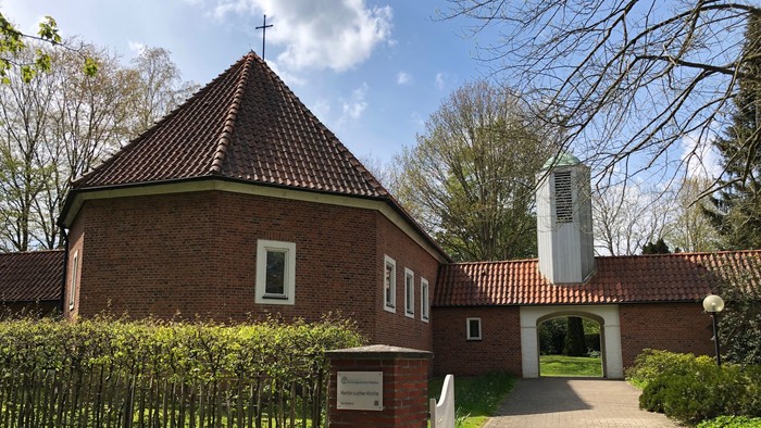 Kirchliche Anlage mit rotem Backsteingebäude und weißem Glockenturm im Hintergrund