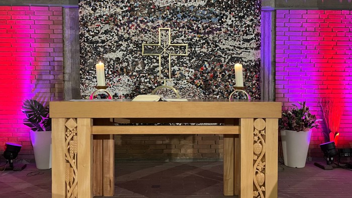 Holztisch mit Kerzen und Pflanzen, bunte Ziegelsteinwand im Hintergrund