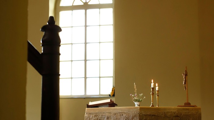 Idyllischer Altar mit Kerzen, Kruzifix und einem gewölbten Fenster, das einen schlichten Steintisch erhellt.