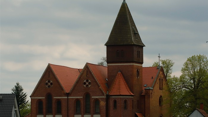 Ein rotes Backsteingebäude mit spitzem Turm und Wetterfahne.