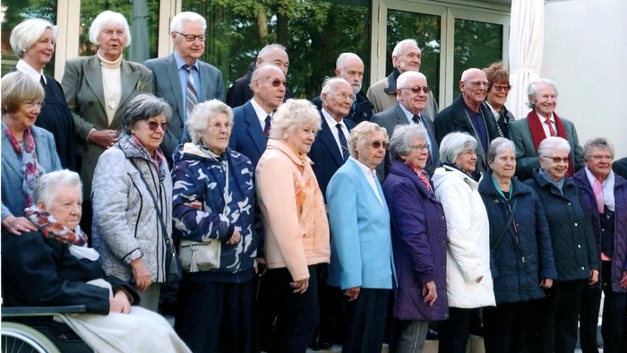 Eine Gruppe älterer Menschen posiert für ein Gruppenfoto, einige stehen, andere sitzen im Rollstuhl