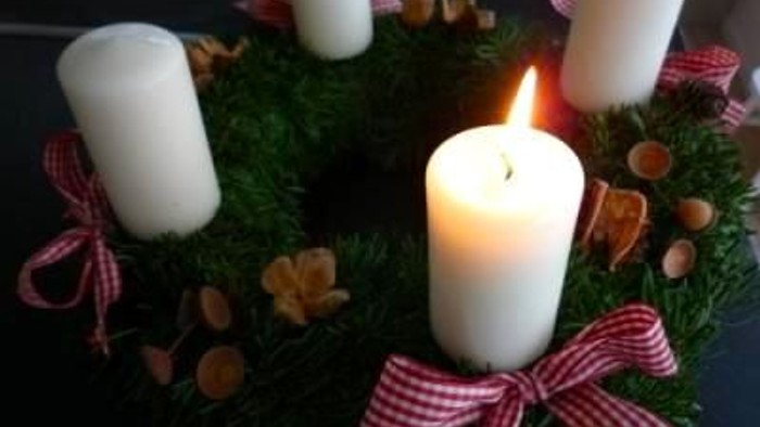 En juledekorasjon med tre lyse lysstaker på en grøn krans med røde bænder og nødder.