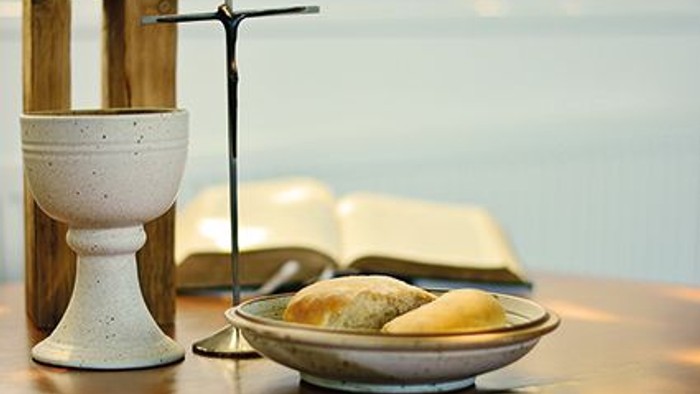 Auf dem Tisch stehen ein Kelch, ein Kreuz und eine Schale mit Brot neben einem aufgeschlagenen Buch