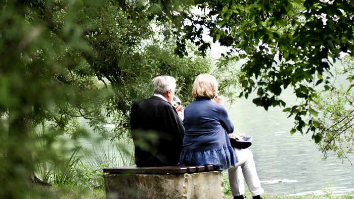 Ein älteres Paar sitzt auf einer Bank am Wasser und schaut in die Ferne.