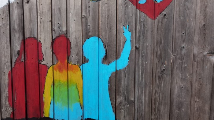 Bunte gemalte Silhouetten mit einem Herz und Discokugeln an einer Holzwand.