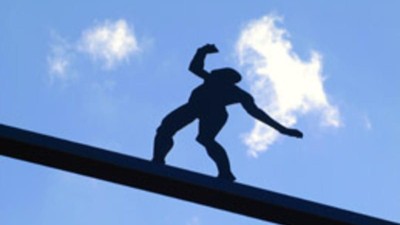 Eine Silhouette eines Mannes auf einem schmalen Geländer vor blauem Himmel.