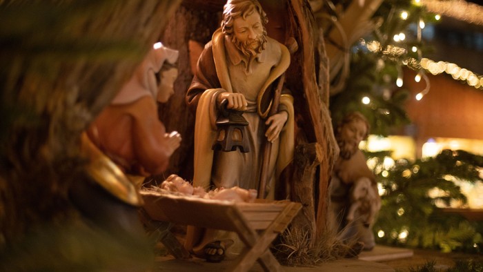 Eine Krippenszene mit Figuren und einem Weihnachtsbaum im Hintergrund.