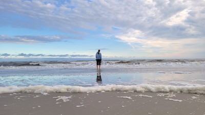 Ein Mann steht am Strand im Wasser und schaut auf den Ozean.